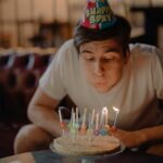 Man celebrating birthday at home blowing out candles on cake.